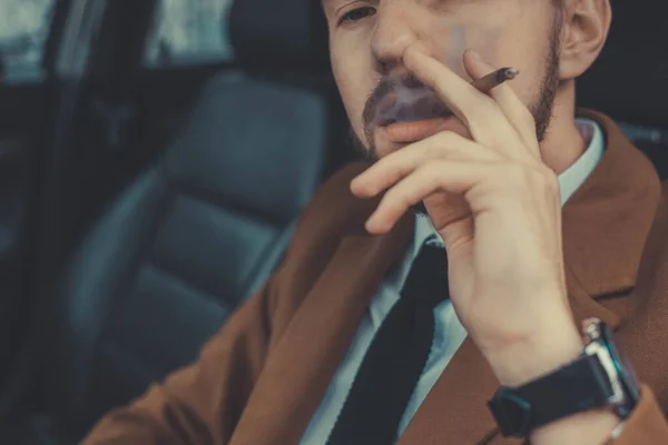 Retrato de un joven de treinta años, de cerca, conduciendo un auto fuma un cigarrillo. Un hombre de negocios con barba en traje de negocios, fuma brutalmente un cigarrillo. En el procesamiento creativo —  Fotos de Stock