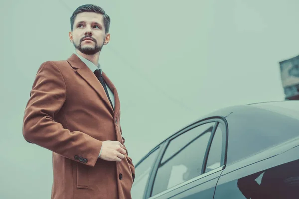 Portret van een jonge bebaarde zakenman van dertig jaar oud. In een zakelijke stijl, staat bij het bedrijf auto, kijken naar de zijkant. Tegen de lucht. In creatief kleuren — Stockfoto