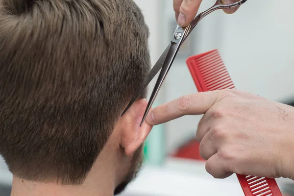 Mäster frisör klipper hår på huvudet på en ung skäggig kille. Närbild av handen på en professionell hårklippare med sax i en frisör butik. — Stockfoto