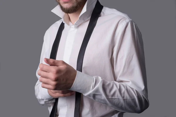 Portrait of a young bearded man, in a white shirt, with an untied tie, holding his hand in a cufflink by the sleeve. On a dark gray background — Stock Photo, Image