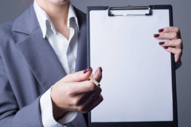 Yakın çekim stüdyo portresi, gri takım elbiseli iş kadını, ceket. Kağıt dolu bir dosyanın içinde imza için arka planı olan bir kalem tutuyordu. Gri bir arkaplanda