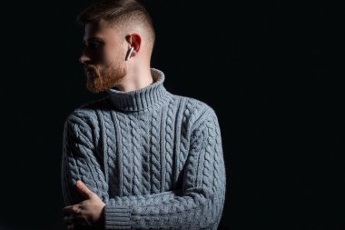 25 yaşında sakallı bir gencin stüdyo portresi. Sıcak bir kazak içinde, gururla, gri, başka tarafa bakıyor. Siyah bir arka planda. dramatik bir sanatsal ışıkta.