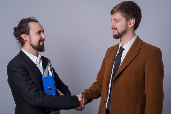 Portrait of two young business people in business suits. handshake. The boss hired a new employee in the team, holding a folder with personal files
