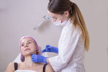 Kozmetik bilimciler ofisinde portre. Tıbbi giysili, eldivenli ve şırıngalı genç bir kız kırışıklıkları tedavi etmek için yüz ve boyun kaslarına iğne yapıyor. Yara izleri, kas spazmı, torticollis.