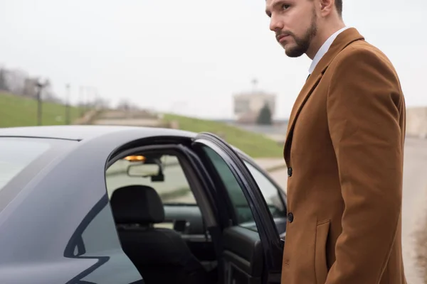 Retrato de un joven en ropa de negocios, un hombre de negocios de treinta años abre la puerta del coche para salir. En una interesante autoría —  Fotos de Stock