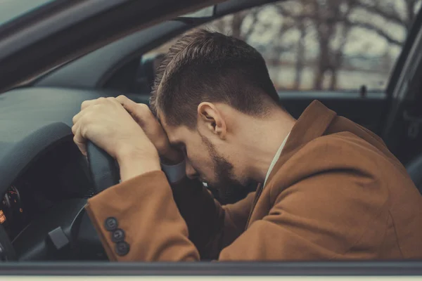 Um jovem de trinta anos, segurando a cabeça, com dor de cabeça, dirigindo um carro. Pobre saúde durante a condução . — Fotografia de Stock