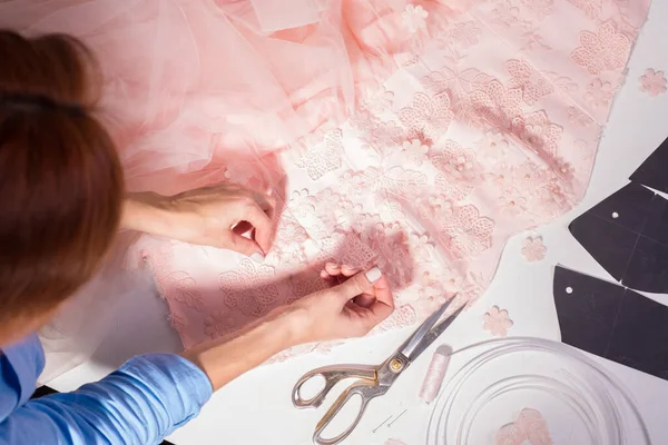 Vue de dessus d'un lieu de travail de couturier dans son atelier de fabrication de vêtements. Vêtements faits main, coud professionnellement des fleurs décoratives sur une robe rose . — Photo