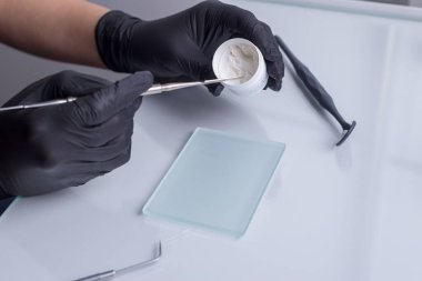 Yakın plan, dişçilerin ellerinin üst görüntüsü, eldivenli, elinde bir hazırlık aleti var. Diğer diş aletlerinin arka planına karşı. Tıbbi düz çizgi.