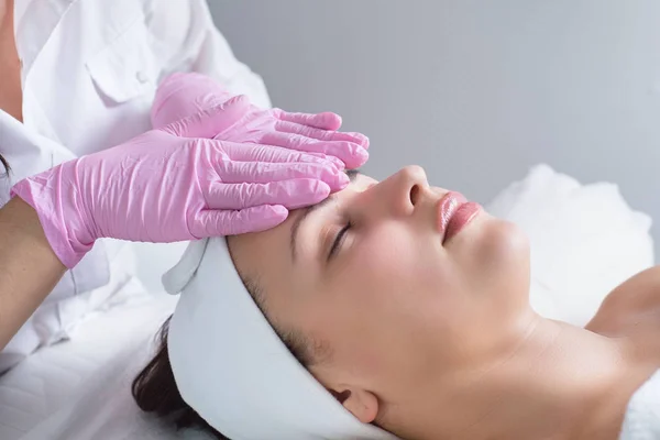 Close-up, retrato de uma jovem menina bonita, com pele impecável, que o mestre massagista faz massagem facial, em luvas médicas. Em um salão de beleza — Fotografia de Stock