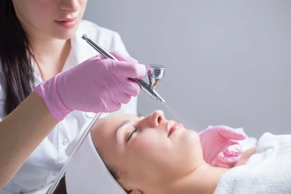 Närbild, händer av en professionell kosmetolog läkare, med hjälp av apparaten, sprutar en kosmetisk produkt, serum, på en ung patients hud. Syresättning av huden i ansiktet. I skönhetssalongen. — Stockfoto