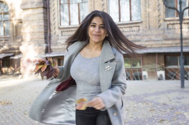 Güzel bir Hintli kızın portresi, gülümseyerek dönüyor, elinde sonbahar yapraklarıyla dans ediyor..
