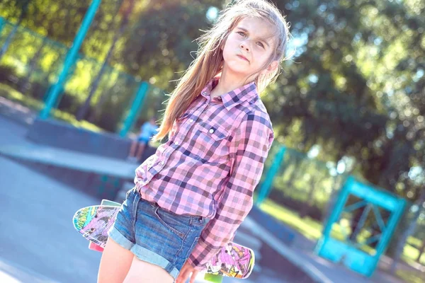 Retrato de una pequeña adolescente, caminando por la calle, sosteniendo un monopatín colorido, estilo de vida activo de los niños — Foto de Stock