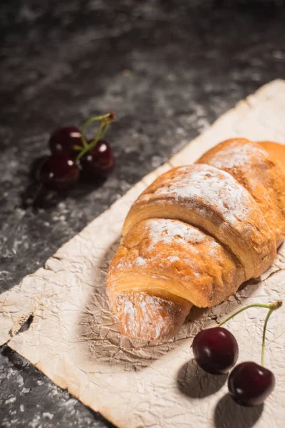 French croissant with cherries and powdered sugar. Rustic style on a dark gray abstract background. — Stock Photo, Image