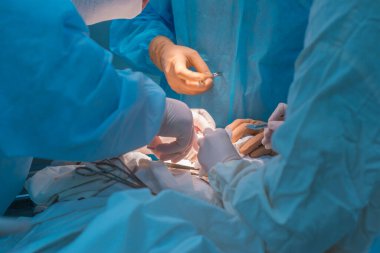 close-up, the hands of pediatric surgeons and an assistant operating a small patient with behind-the-ear lymphadenitis. In a sterile operating room. Removing a malignant tumor of the ear with a scalpel, suturing soft tissues, electrocoagulation, stop