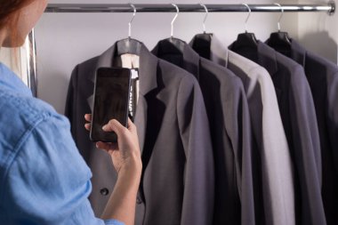 Giyim mağazasında iş ceketleri olan bir tezgah. Boş alan. Erkek ve kadın takım elbise dükkânı. Elbise satıcısı kız akıllı telefon fotoğraflarıyla bir giyim mağazasında kaliteli iş ceketleriyle bir tezgah