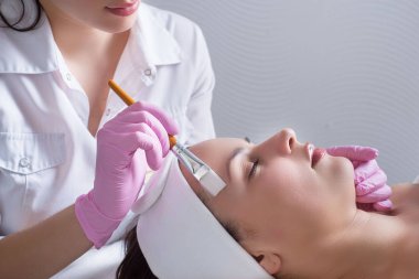 close-up, hands of a professional cosmetologist doctor, using a tool, performs the application of cream and oil on the skin of the face of a young patient. In the beauty salon. Treatment of facial skin diseases. Beauty and skin care. Healthy facial s