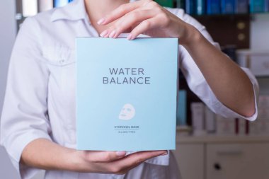 Zaporozhye. Ukraine January 2020. Beauty Salon Prima Vera. Girl beautician in defocus, keeps in focus cosmetic means for body care, company water balance in the background cosmetics
