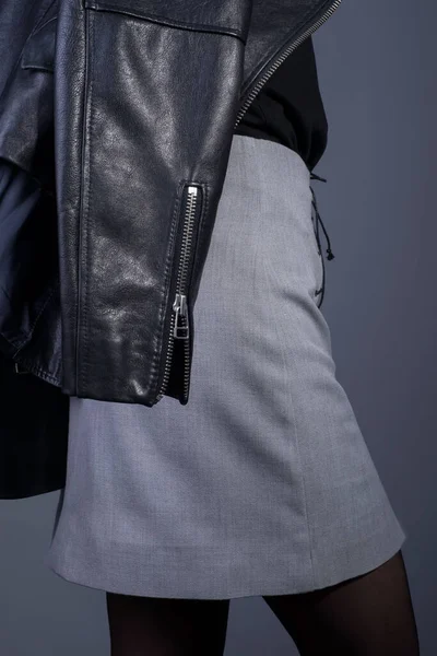 In the catalog of photo advertising, the model is dressed in a gray skirt and a leather jacket in the style of rock and roll, close-up. On a gray background. Catalog for an advertising magazine. High quality leather jacket. Gray designer skirt.