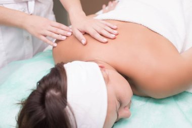 Masör bir kızın elleri, kaplıca salonunda genç bir kadına sırt masajı yapıyor. Cilt masajı, sırt kasları, boyun omurgası, tasma bölgesi. Manüel terapi. Omurga hastalıklarının masajla tedavi edilmesi