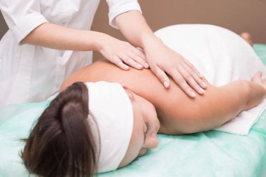 Masör bir kızın elleri, kaplıca salonunda genç bir kadına sırt masajı yapıyor. Cilt masajı, sırt kasları, boyun omurgası, tasma bölgesi. Manüel terapi. Omurga hastalıklarının masajla tedavi edilmesi