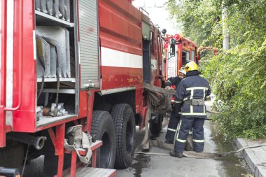 İtfaiye bir konut binasındaki ateşleme kaynağında çalışıyor. Üniformalı insanlar yangın hortumunu açıp yangını söndürmek için hazırlayacaklar. Gösteriş