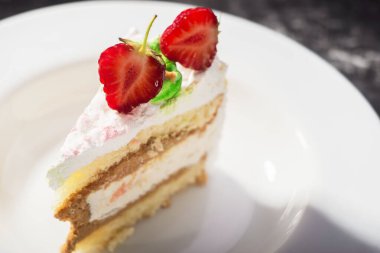 Pasta, pasta, kremalı ve çilekli. Beyaz bir plaka içinde, koyu soyut bir arkaplanda. Yemek fotoğrafı. Dramatik ışık