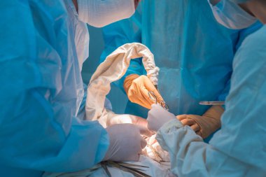close-up, the hands of pediatric surgeons and an assistant operating a small patient with behind-the-ear lymphadenitis. In a sterile operating room. Removing a malignant tumor of the ear with a scalpel, suturing soft tissues, electrocoagulation, stop