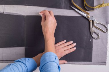 Elbise imalatı ve dikiminde bir ustanın el işçiliğinin en üst görüntüsü. Bir kalem ve cetvel ile tasarımcı kız terzi elbiseleri ve ceketler için kumaş kesiminin sınırlarını işaretler.