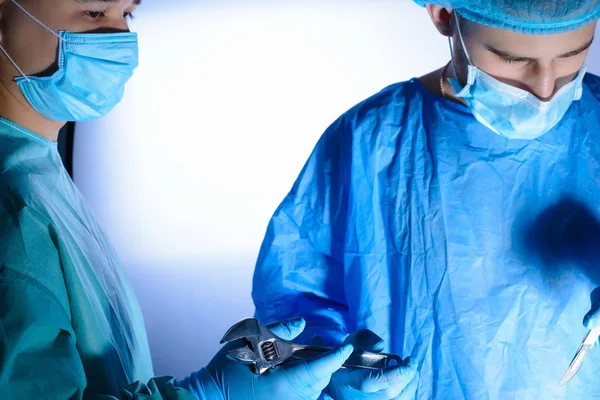 close-up, portrait of two surgeons, in medical masks and a sterile gown. the assistant passes the wrench to the surgeon. Medical humor. Surgical joke. Operating lamp. Sterile operating room. Medical concept