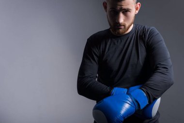 Spor giyimli yakışıklı, vahşi bir adamın dramatik spor portresi. Dövüş pozisyonu almış, boks eldivenlerini çıkarıyor. Gri bir arka planda. Spor yaşam tarzı. Boks, karate, dövüş sanatları, Mma, Conor Mcgregor, savaş çığlığı, eldivenli adam. Dramatik spo
