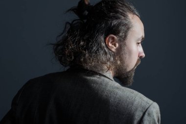 30 yaşında, kıvırcık, yağlı saçlı ve ceketli, sakallı bir gencin dramatik bir portresi. Gri bir arka planda. Saç yıkamama kavramı. Kirli saçlar. Dramatik ışık. Uzun saçlı bir adamın promosyon fotoğrafı. Saç ve kafa derisi. 