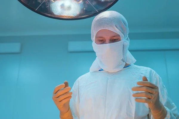 close-up of surgeons in a sterile mask, against the background of an operating lamp, with raised hands, the surgeon's assistant looks at the indicators in a monitor, sterile gloves and a mask. Pediatric surgery in Ukraine. Sterile conditions, medical