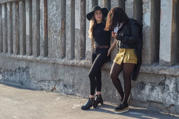 Plan general de dos hermosas chicas españolas jóvenes, generación Y, están de pie en el viejo muro de textura, sonriendo — Foto de Stock