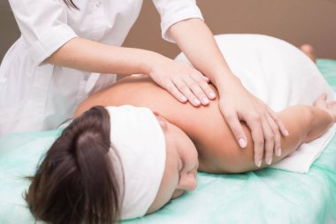 Masör bir kızın elleri, kaplıca salonunda genç bir kadına sırt masajı yapıyor. Cilt masajı, sırt kasları, boyun omurgası, tasma bölgesi. Manüel terapi. Omurga hastalıklarının masajla tedavi edilmesi
