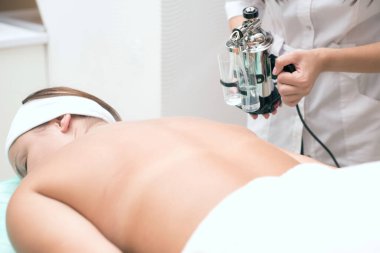 Profesyonel bir kozmetik uzmanı genç bir hastanın sırtına gerekli yağı püskürten bir cihaz kullanıyor. Güzellik salonunda spa tedavisi. Vücut bakımı. Cihaz gerekli yağların püskürtülmüş hali. Kozmetolojide modern teknolojiler