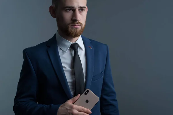ザポロジー ウクライナだ 2020年2月 ビジネススーツに身を包んだ若い髭の男がIphone Xを手にしている姿がクローズアップされている Appleの新しいスマートフォン ビジネスにおける近代的な技術 ビジネスマンはアップルの新しいスマートフォンで話している — ストック写真