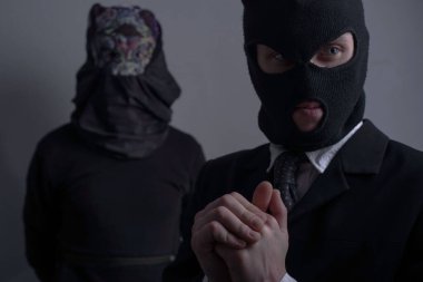 Yakın çekim stüdyo portresi, iki soyguncu. Siyah maskeli bir haydut, ön planda bir ceket, arka planda korkunç maskeli başka bir soyguncu. Gri bir arka planda. Organizasyon. Yaklaşan suçlar. Siyah elbiseli insanlar.,