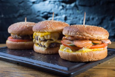 Tahta masada taze burger yakın plan. Ağız sulandırıcı yazarın berger fotoğrafında shiemgo, peynir ve sığır köftesi gibi çeşitli tatlar var. Taştan bir duvarın karanlık arka planında, kırsal bir tarzda. Yiyecek ve içecekler. Teşekkürler.