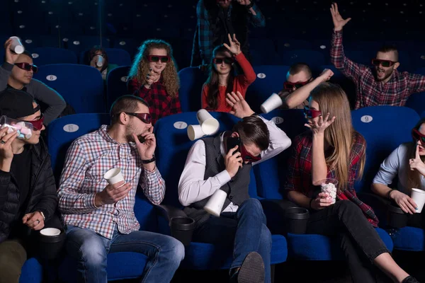 The general plan of young people of different sexes, from nineteen to thirty years. A group of people throw paper cups on a guy talking on a smartphone in a movie theater. stopping people from watching a movie. Generation Z, Generation Y, Millennials