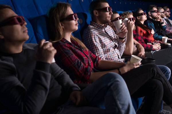 a group of young people of different sex, sitting in chairs in the cinema, watching a movie, eating popcorn. In glasses for 3D. Private screening of the film. Young people of different generations, including millennials, generation Z, Y. Girls and bo