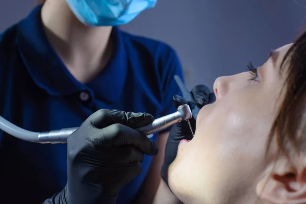 close-up, from an unusual angle, view, a dentist using dental equipment treats a patient a girl with a tooth and oral cavity disease. In the dental office. Prevention and treatment of diseases of the oral cavity and teeth. Diagnosis of caries, period
