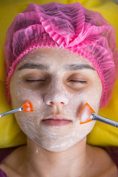 close-up, hands of a professional cosmetologist doctor, using brushes applying a cosmetic natural mask on the skin of the face of a young beautiful patient. Oxygenation of the skin of the face. In the beauty salon. Treatment of facial skin diseases.