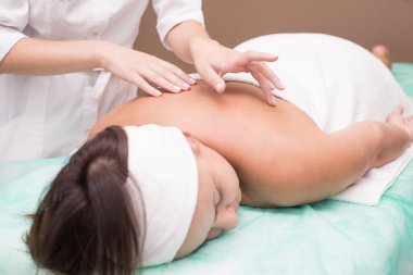 Masör bir kızın elleri, kaplıca salonunda genç bir kadına sırt masajı yapıyor. Cilt masajı, sırt kasları, boyun omurgası, tasma bölgesi. Manüel terapi. Omurga hastalıklarının masajla tedavi edilmesi