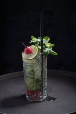 Siyah arka planda taze kuyruk, hafif alkollü bir kokteylin reklam çekimi, bir tutam nane, krema şekeri, dekoratif üzüm çileği. Kaba bir şekilde, karanlık bir arka planda. Parlak resimler için ilginç bir reklam..