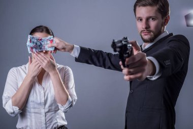 Genç sakallı bir adamın stüdyo portresi, bir eliyle tabancasını tutuyor, diğer eliyle gözlerini kapatıyor ve genç bir kıza, işlenen suç hakkında sessiz kalması için para veriyor. Gri bir arka planda. Suç komisyonu. Hesaplaşma, suçu gizleme,