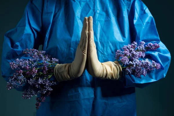 lilac flowers grow from under doctor gloves. Medical concept. The doctor holds yellow flowers in a sterile glove and a blue work suit. Health and healthcare. Operation. Yellow flower. On a blue background. Beauty and health. Aesthetic medicine