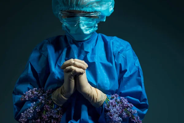 lilac flowers grow from under the doctors gloves. Prayer of a nurse. Medical concept. Doctor holds yellow flowers in a sterile glove and a blue work suit. Health and healthcare. Operation. Yellow flower. On a blue background. Health and beauty. Aesth