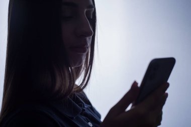 Elinde yeni bir akıllı telefon tutan 22 yaşındaki bir kızın stüdyo portresi. Reklam fotoğrafı çok parlak. Modern akıllı telefon ve gençler. Kız yeni bir akıllı telefon kullanıyor. Mutlu akıllı telefon sahipleri. Yeni bir smar ile bir kızın koyu portresi