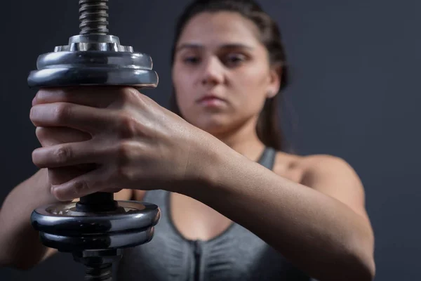 スポーツ女性のダンベルの肖像画と筋肉を汲み上げる若い運動女性はダンベルで運動をしています グレーの背景にスタジオ写真 スポーツと健康 積極的なライフスタイル アスレチックガールはダンベルの手の筋肉を振る — ストック写真