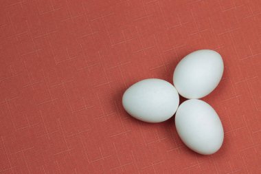 Kırmızı arka plana yerleştirilmiş üç beyaz yumurta. Paskalya süslemeleri.